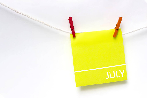 Július. Hónap, naptár hónap. Papír kártyák naptári nap lóg kötél ruhacsipeszekkel fehér háttér. Nyár, az év hónapja koncepció - Fotó, kép