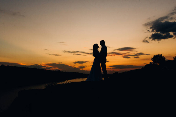 silhouettes of a happy young couple guy and girl on a background of orange sunset in the ocean - Foto, Imagen