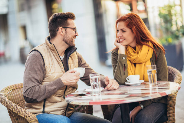 Ελκυστικό νεαρό ζευγάρι ερωτευμένο να κάθεται στο τραπεζάκι του καφέ έξω, πίνοντας καφέ - Φωτογραφία, εικόνα