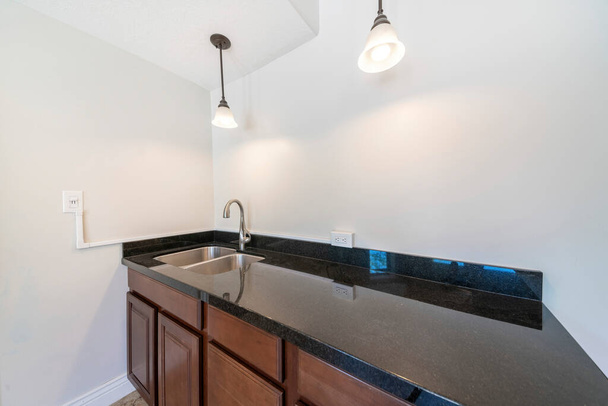 Mutfak lavabosu siyah granit kapaklı ve koyu ahşap çekmeceler ve dolaplarla dolu. - Fotoğraf, Görsel