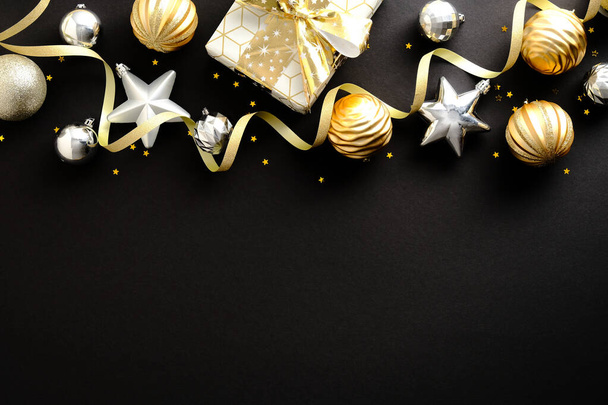 Christmas composition. Golden and silver Christmas stars and balls decoration, gift box on dark black background. Christmas or New Year greeting card design. Flat lay, top view, copy space. - Photo, image