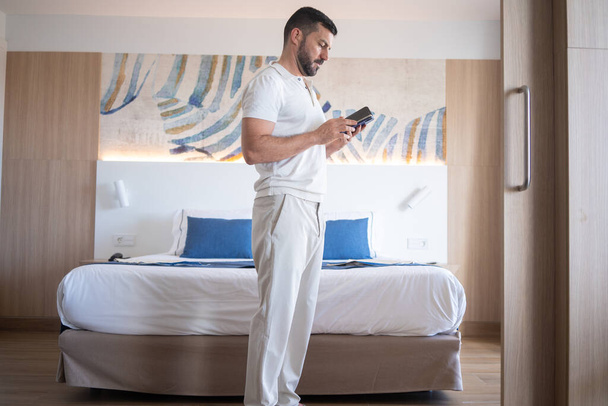  attraente uomo seduto in camera d'albergo guardando mobile. - Foto, immagini