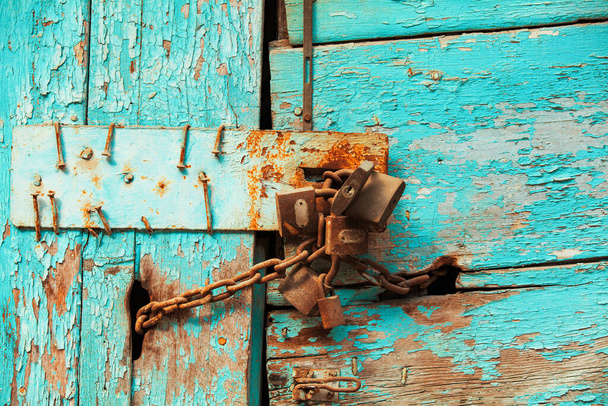 Photo rapprochée de cadenas rouillés enchaînés sur une porte en bois usée avec peinture bleue épluchante.  - Photo, image