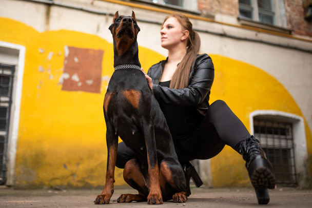 A girl in leather, with a Doberman, in an old yard. High quality photo - Photo, Image