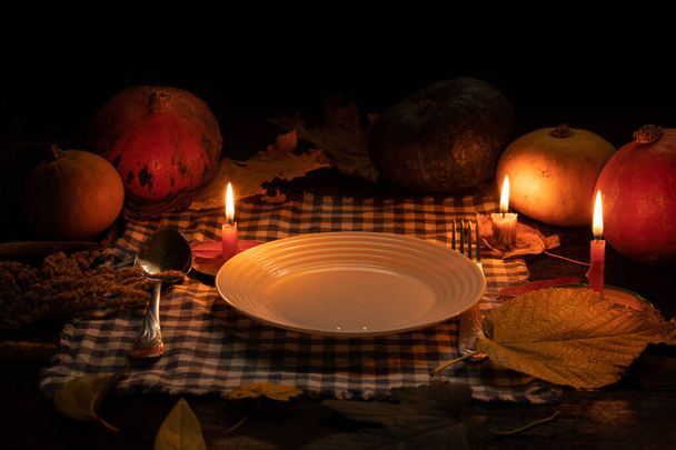 un plato vacío está sobre la mesa a la luz de las velas sobre un fondo de calabaza y hojas de otoño, cena a la luz de las velas, decoración de la mesa de otoño, mesa festiva a la luz de las velas - Foto, Imagen
