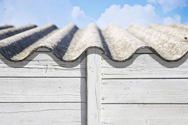 Altes gefährliches Dach aus gewellten Asbestplatten über einer Holzkonstruktion - eines der gefährlichsten Materialien in der Bauindustrie, der so genannte versteckte Killer - Foto, Bild