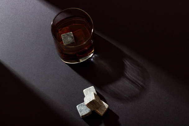 Transparent glass with whiskey on a dark background with bright rays of light. Whiskey stones in a glass glass - Fotó, kép
