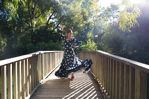 hermosa bailarina española morena flamenca con un traje de flamenca típico con lunares blancos bailando en una pasarela de madera en la calle. Patrimonio cultural flamenco de la humanidad. - Foto, imagen