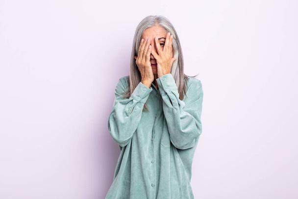 middle age gray hair woman covering face with hands, peeking between fingers with surprised expression and looking to the side - Foto, Imagem