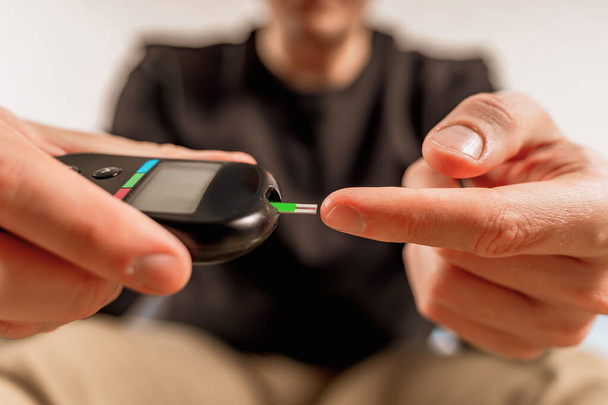 Een man thuis gebruikt een glucosemeter om de bloedglucose te meten. Een vinger doorboren met een naald - Foto, afbeelding