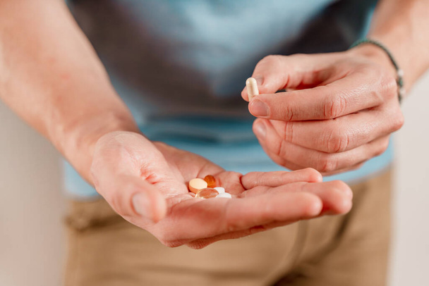 El hombre tiene pastillas y cápsulas en la mano. Tomar vitaminas y medicamentos, de cerca - Foto, Imagen