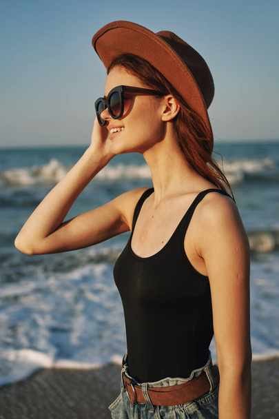 mujer alegre en gafas de sol y un sombrero por el océano caminar verano - Foto, Imagen
