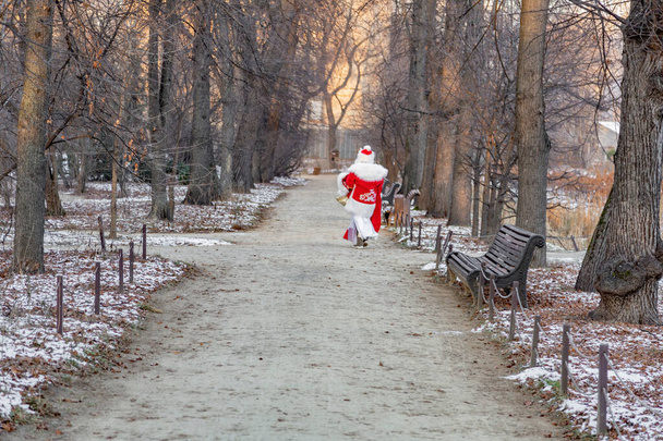 Ein Mann im roten Nikolausanzug geht in einem Winterpark einen Pfad entlang - Foto, Bild