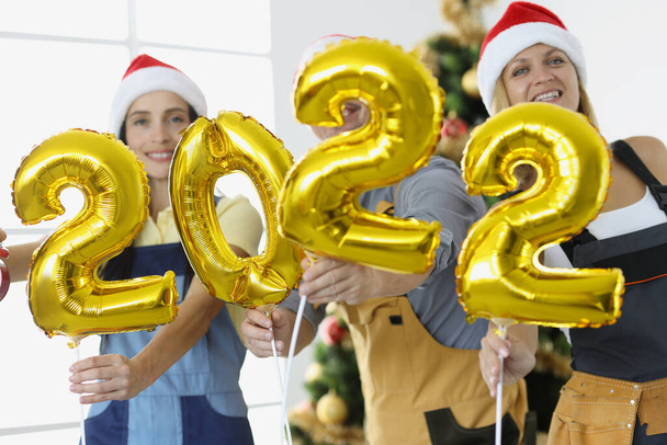 Команда людей у формі тримає цифри 2022 на тлі новорічної ялинки
 - Фото, зображення