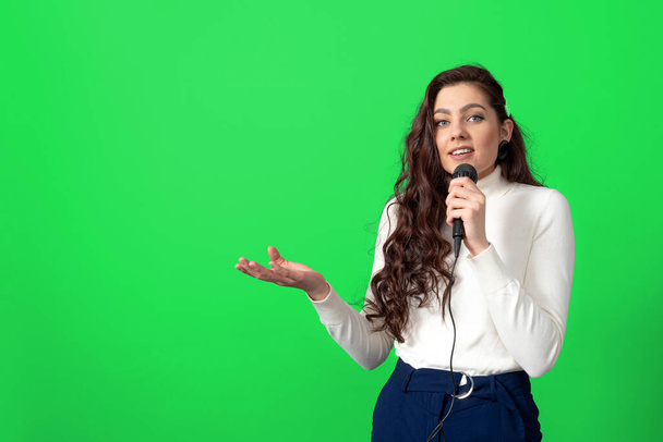 attractive female conference speaker during presentation, holds microphone and makes some gestures, isolated on green - Photo, image