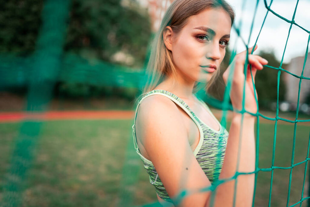 Beautiful fitness girl with who stands behind the net of the goal - Photo, Image