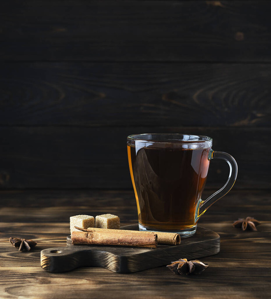 Fragrant hot tea with cinnamon in a transparent cup on a dark brown wooden board - Foto, Bild