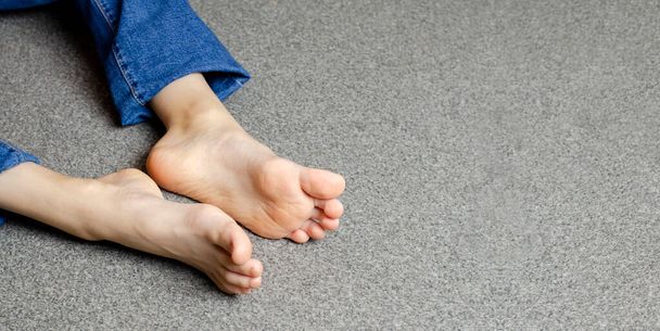 Child's bare feet. Girl's legs in jeans. Sitting on the floor. - Fotoğraf, Görsel