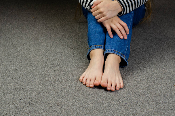 Los pies desnudos del niño. Piernas de niña en jeans. Sentado en el suelo. - Foto, imagen