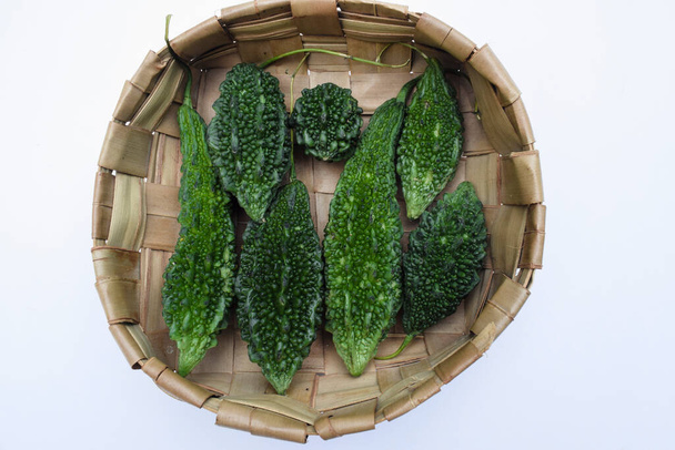 Горькие или горькие дыни, сложенные в корзине. Зеленые овощи различных размеров Карела в плетеной корзине с деревянным фоном - Фото, изображение