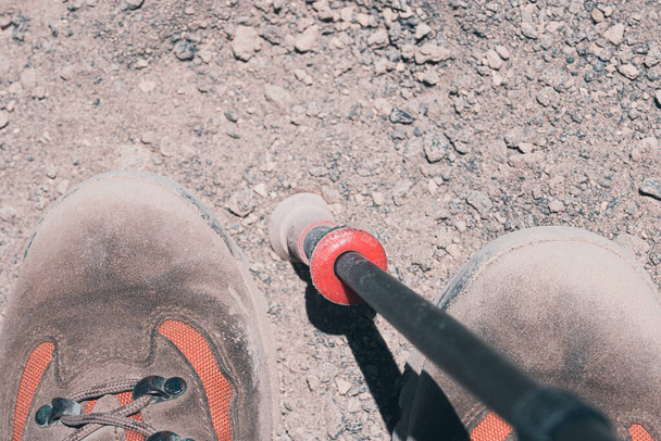 Un fragmento de botas de trekking polvorientas en el sendero y el bastón de trekking en un día soleado. - Foto, imagen