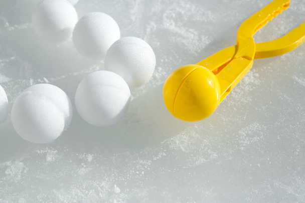 Uma ferramenta para modelar e fazer bolas de neve de neve para jogos infantis de inverno. Bolas de neve deitadas no gelo congelado ao lado de um instrumento de plástico brilham nos raios do sol. Bola de neve Tongs.frozen água - Foto, Imagem