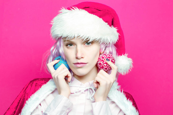Young woman or cute girl in christmas santa hat holds Christmas balls on pink background. Closeup face portrait - Foto, Bild