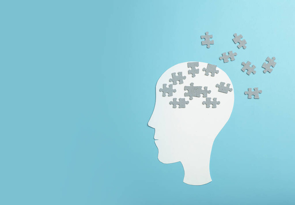 Dementie, Alzheimer, geheugen en mentale gezondheid concept achtergrond. Papieren hoofd met puzzelstukjes op een blauwe achtergrond - Foto, afbeelding