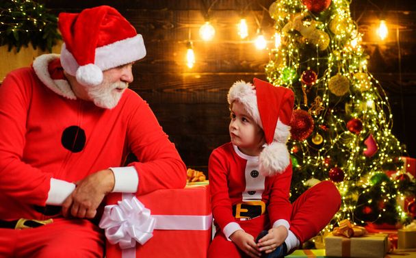 サンタクロースとクリスマスプレゼント付きの小さなサンタの男の子。家族の休日だ。クリスマスプレゼント。明けましておめでとうございます. - 写真・画像