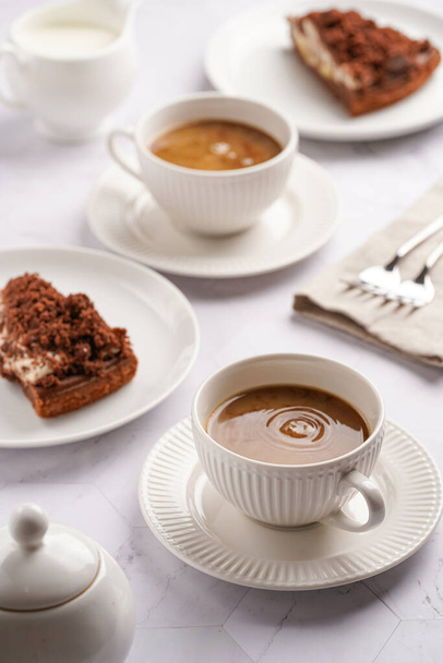 sweet breakfast - two white porcelain cups with coffee drink cappuccino with milk on a white saucer, piece of brown cake - Zdjęcie, obraz