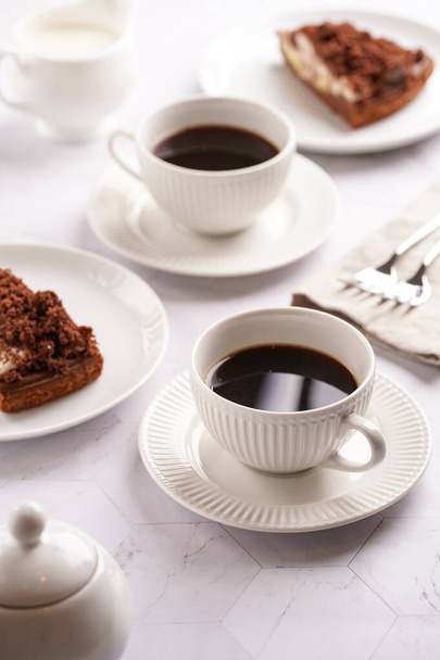 petit déjeuner sucré - deux tasses en porcelaine blanche avec boisson au café sur une soucoupe blanche, morceau de gâteau brun - Photo, image