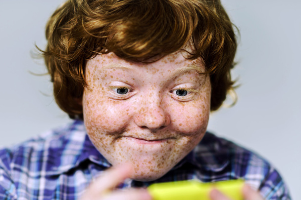Comic freckled red-haired boy with mobile phone - 写真・画像