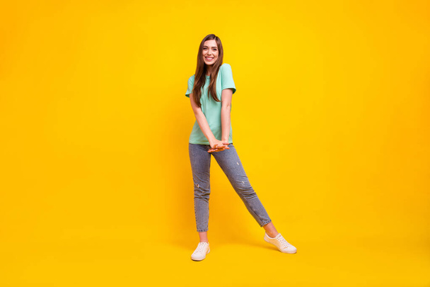 Full size photo of cute brunette hairdo millennial lady stand wear t-shirt jeans sneakers isolated on yellow background - 写真・画像