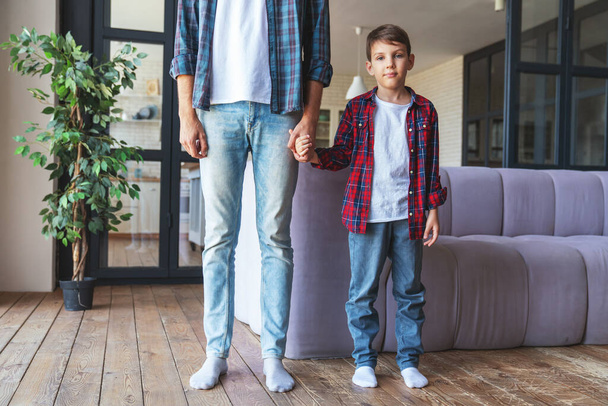 Retrato de un niño de pie junto a su padre con una sonrisa en casa en la sala de estar. - Foto, Imagen