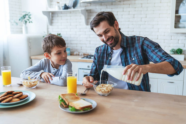 Портрет маленького хлопчика і його тата сидить за столом під час сніданку вдома на кухні
. - Фото, зображення