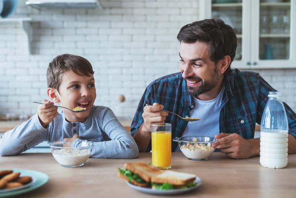 Retrato de um menino e seu pai sentados à mesa durante o café da manhã em casa na cozinha. - Foto, Imagem