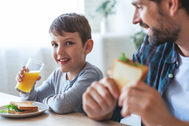 Retrato de um menino e seu pai sentados à mesa durante o café da manhã em casa na cozinha. - Foto, Imagem