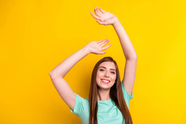 Photo of optimistic brunette hairdo young lady hands up wear teal t-shirt isolated on yellow color background - 写真・画像