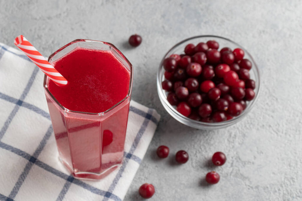 One glass with homemade freshly cranberry juice and a bowl of cranberries on a gray concrete table - Foto, Imagem