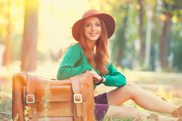 όμορφη κοκκινομάλλα κοπέλα με βαλίτσα στο πάρκο. - Φωτογραφία, εικόνα