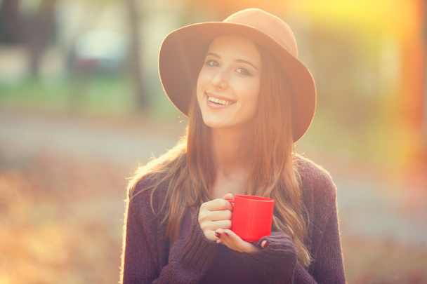 Beautiful redhead girl with cup in the park. - Photo, Image