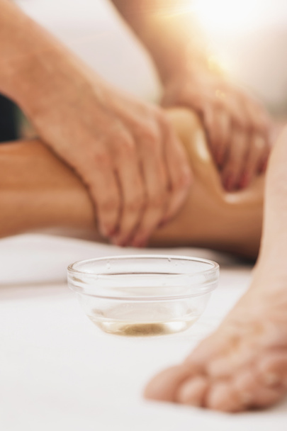 Masaje anti celulitis en las piernas. Masajista aplicando aceite natural de masaje de abedul en piernas femeninas bronceadas - Foto, Imagen