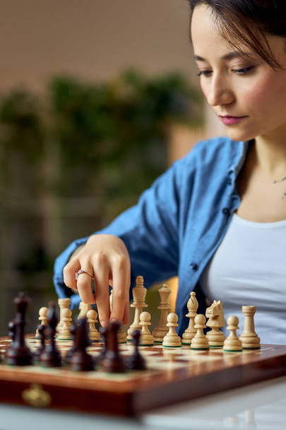 Giovane donna che muove i pezzi di scacchi sulla scacchiera mentre gioca a scacchi a casa da sola - Foto, immagini