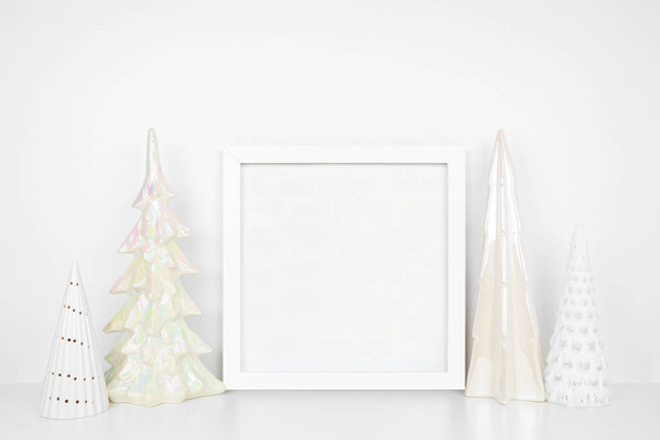 Christmas mock up with white frame and shiny glass tree decor. Square frame on a white shelf against a white wall. Copy space. - Photo, Image