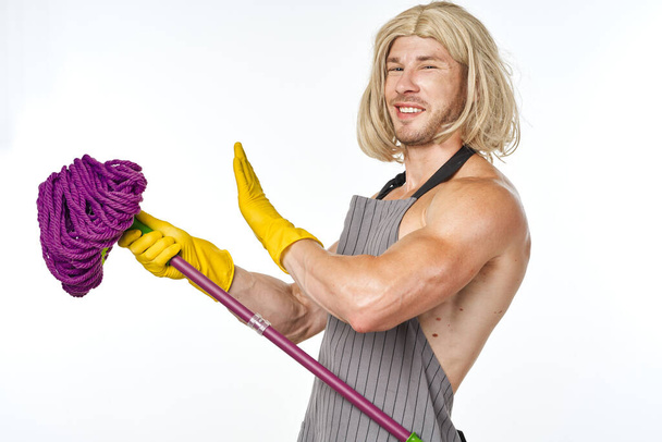 muscular man in apron with a mop in a womans wig - Fotoğraf, Görsel