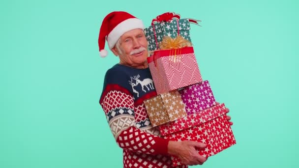 Зрелый дедушка в рождественском свитере держит много подарочных коробок - Кадры, видео