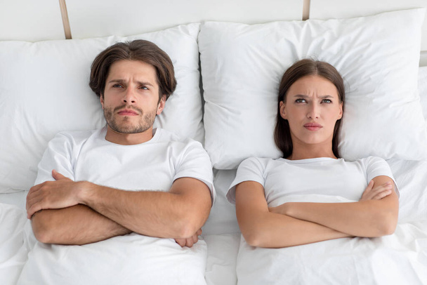 Unhappy offended sad angry millennial caucasian husband and wife with crossed arms on chest lie at white bed - Foto, imagen