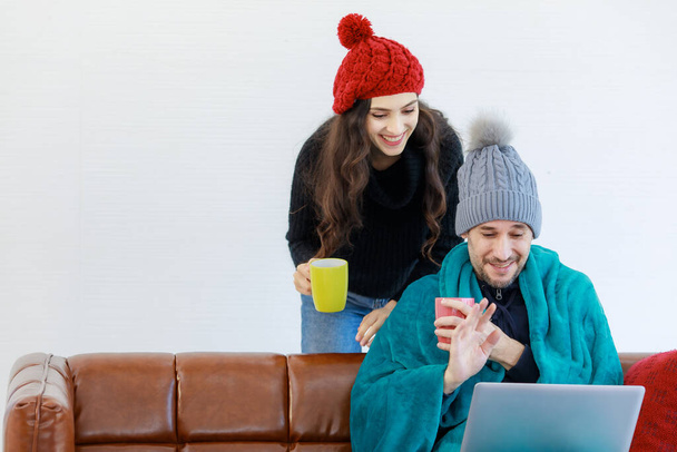 Caucasian boyfriend and girlfriend lover couple in wool sweater jacket and knitted hat cover by blanket drink hot coffee hold hands up say hi greeting friends from laptop computer online video call. - Foto, Imagem