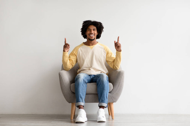 アイデアコンセプト。興奮した黒人男が椅子に座って指を指差す - 写真・画像