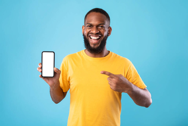Opgewonden Afro-Amerikaanse man presenteert smartphone met leeg scherm, biedt ruimte voor website of app, mockup - Foto, afbeelding